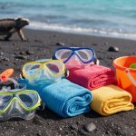 Máscaras de snorkel, toallas y baldes sobre una playa de arena volcánica de Galápagos
